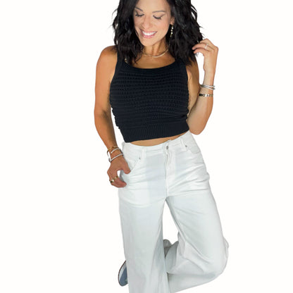 Woman wearing a knit black tank with white pants on a white background