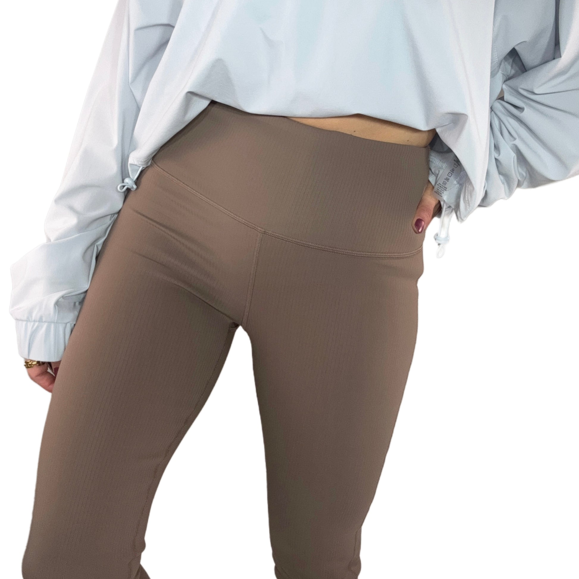 Side profile of a woman wearing ribbed deep taupe leggings, a cropped light blue sweatshirt, on a white background.