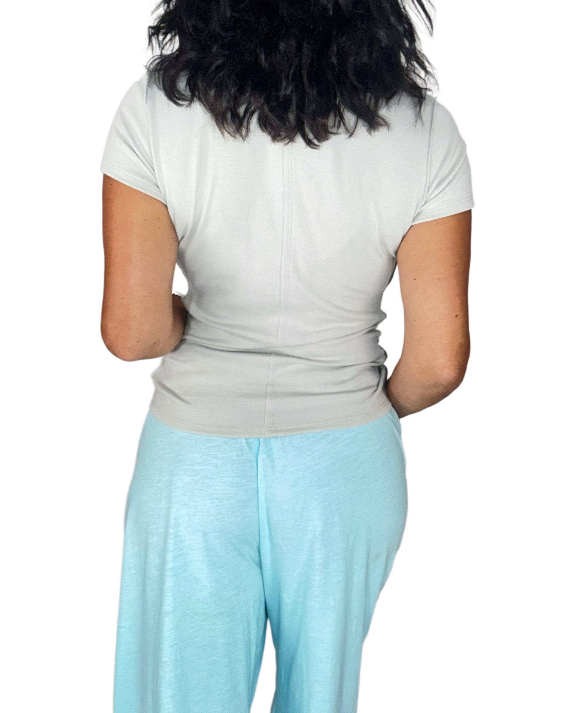 Back profile on a woman wearing a soft grey tee with blue sweatpants on a white background