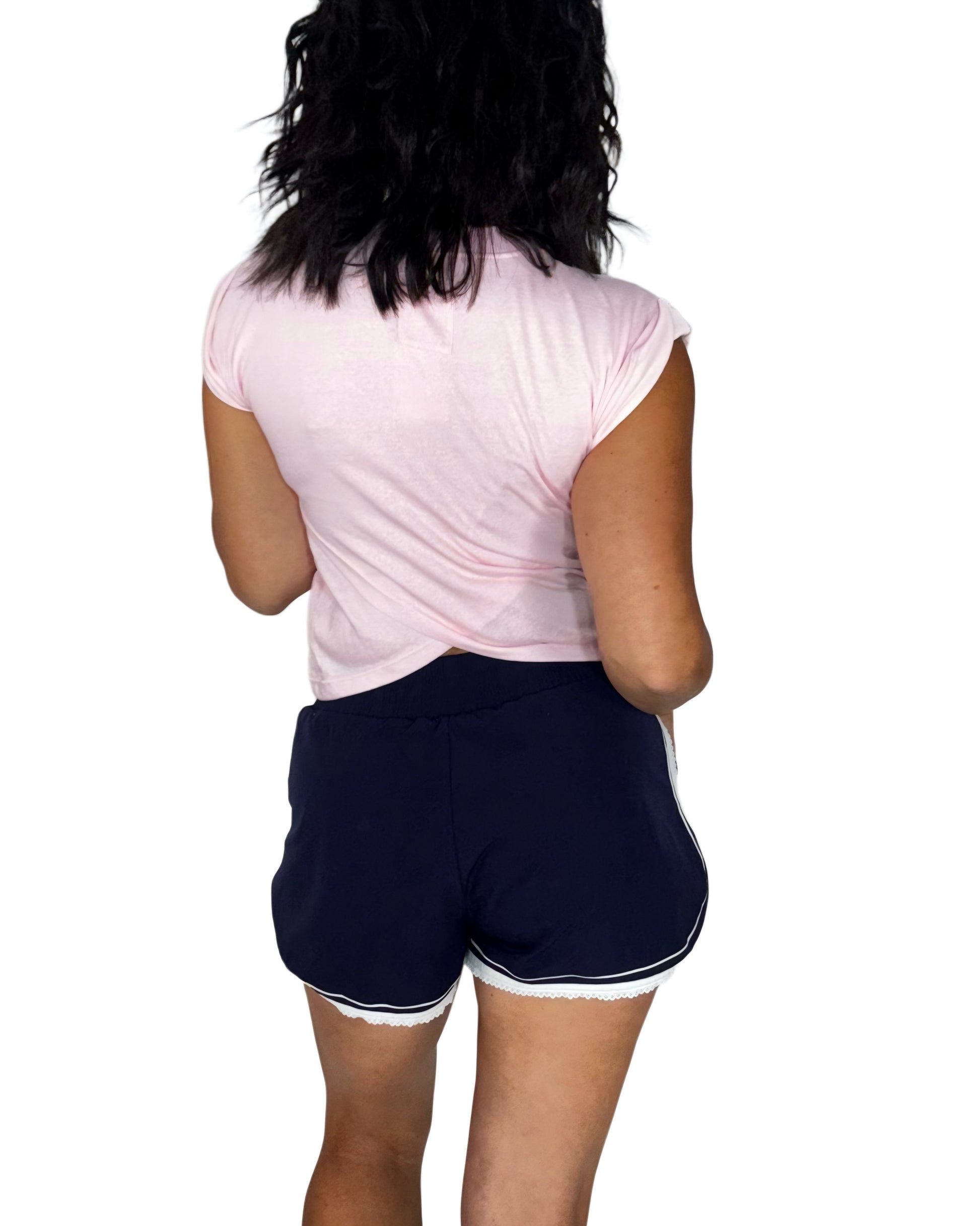 Back profile of a woman wearing navy active shorts with a pink tee, on a white background