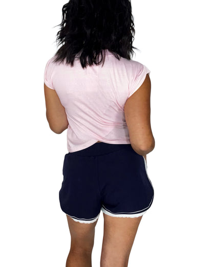 Back profile of a woman wearing a light pin cotton top, with navy active shorts, trimmed with white, on a white background