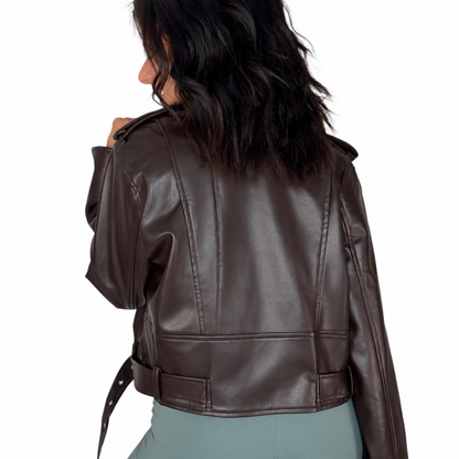 Back profile of a woman wearing a chocolate faux leather biker jacket with light green pants, on a white background  