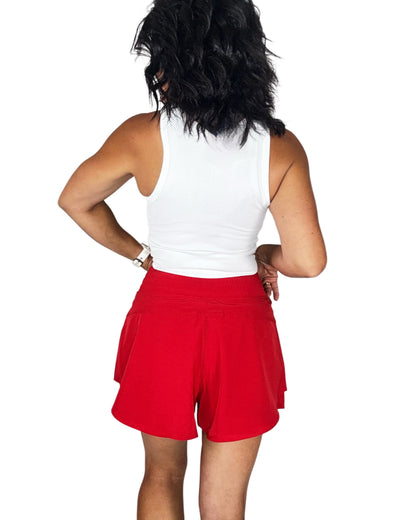 Person wearing a white sleeveless top and red shorts on a white background