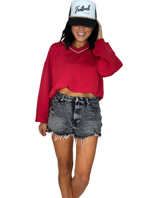 Woman wearing a red crop top, black denim shorts, and a white and black snap back hat with text on a white background