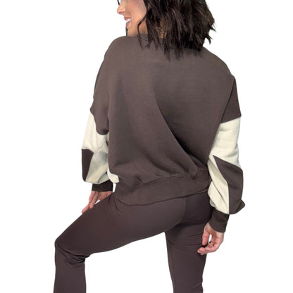 The back of a woman wearing a brown and cream color-blocked outfit on a white background