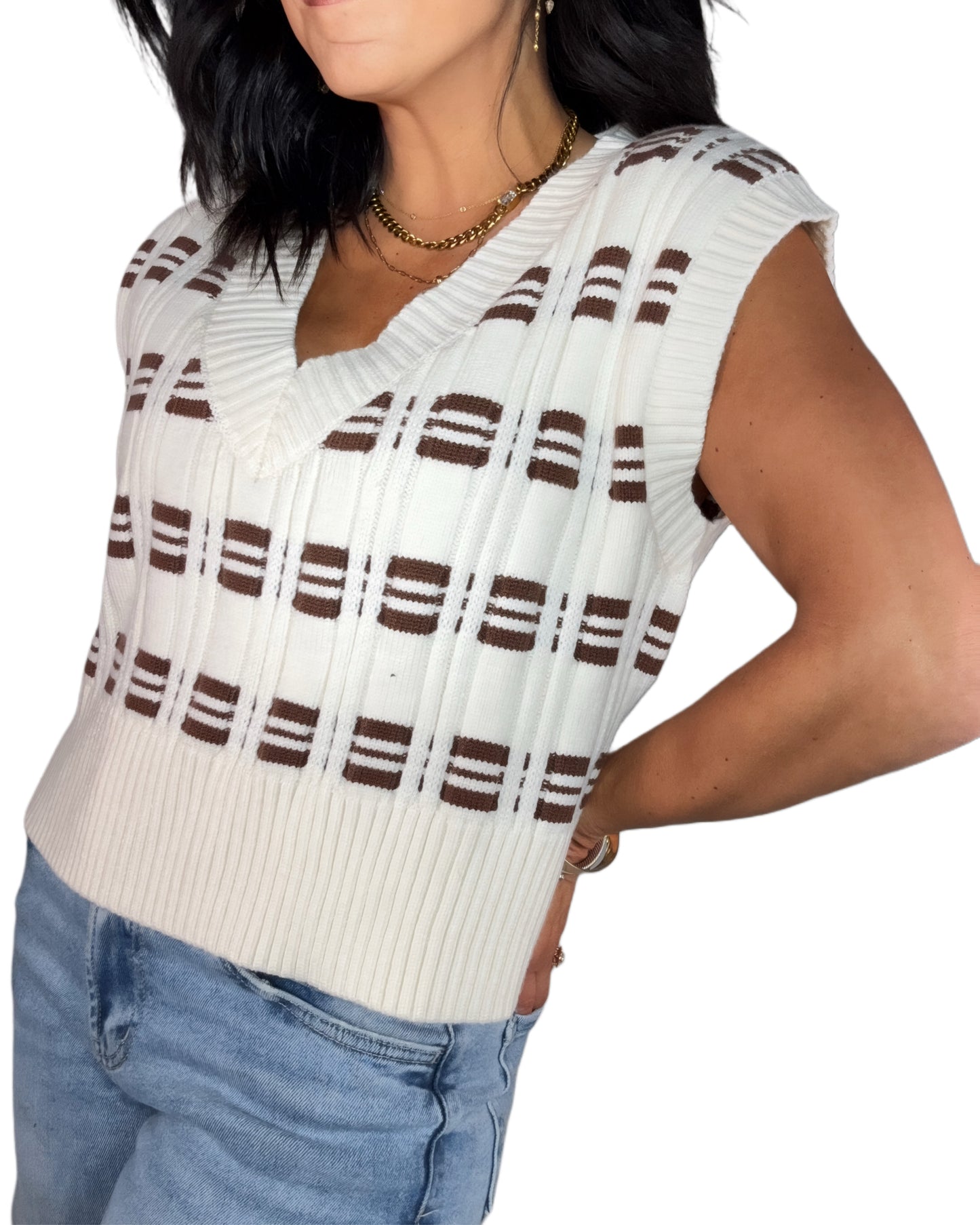 Side profile of a woman  wearing a white and brown striped sweater vest with blue jeans on a white background