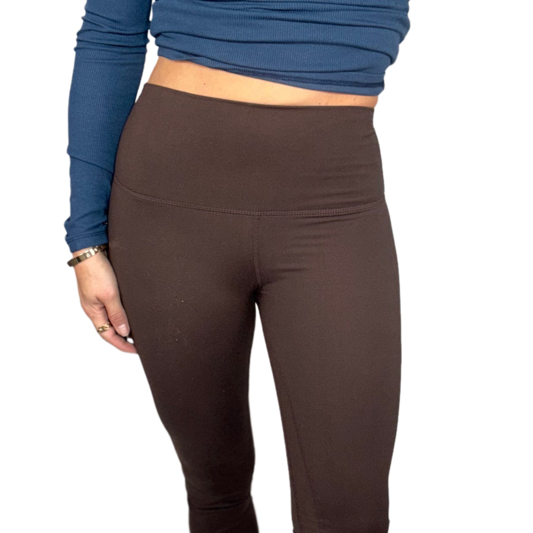 Close up of a woman wearing brown leggings worn with a blue long-sleeve top on a white background