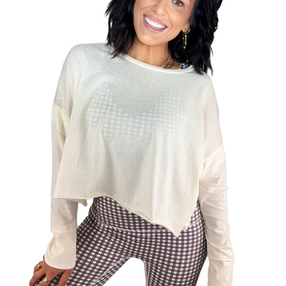 Woman wearing a sheer cream long-sleeve top and checkered pants on a white background