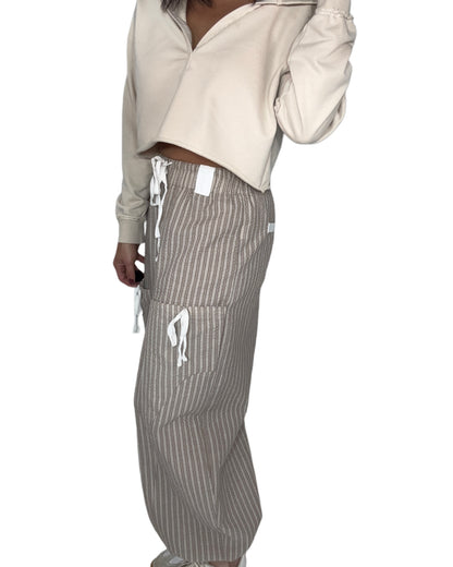 Side profile of a woman wearing a beige cropped hoodie and striped pants on a white background