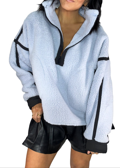 Light blue sherpa pull over with black accents worn by a woman, on a white background