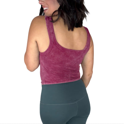Back side of a woman wearing a maroon ribbed athletic top and green leggings on a white background