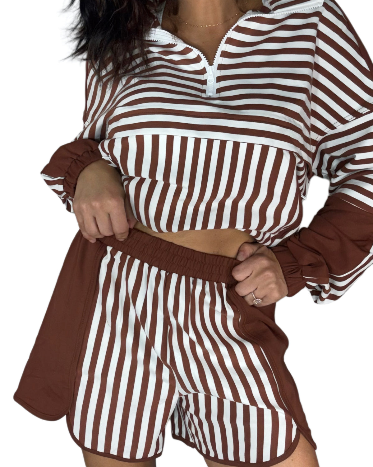 Close up of a woman wearing a brown and white vertically striped two-piece lounge set with a half-zip long-sleeve top and matching shorts, shown against a plain white background.