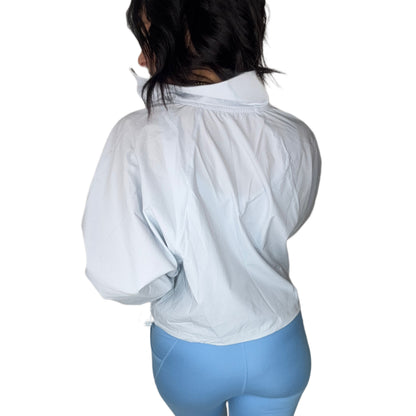 Back profile of a woman wearing a light blue windbreaker pullover with powder blue leggings and a white background