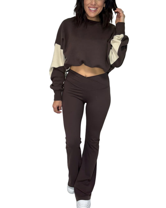 Woman wearing a brown and beige color-blocked sweatshirt and brown flared active pants on a white background