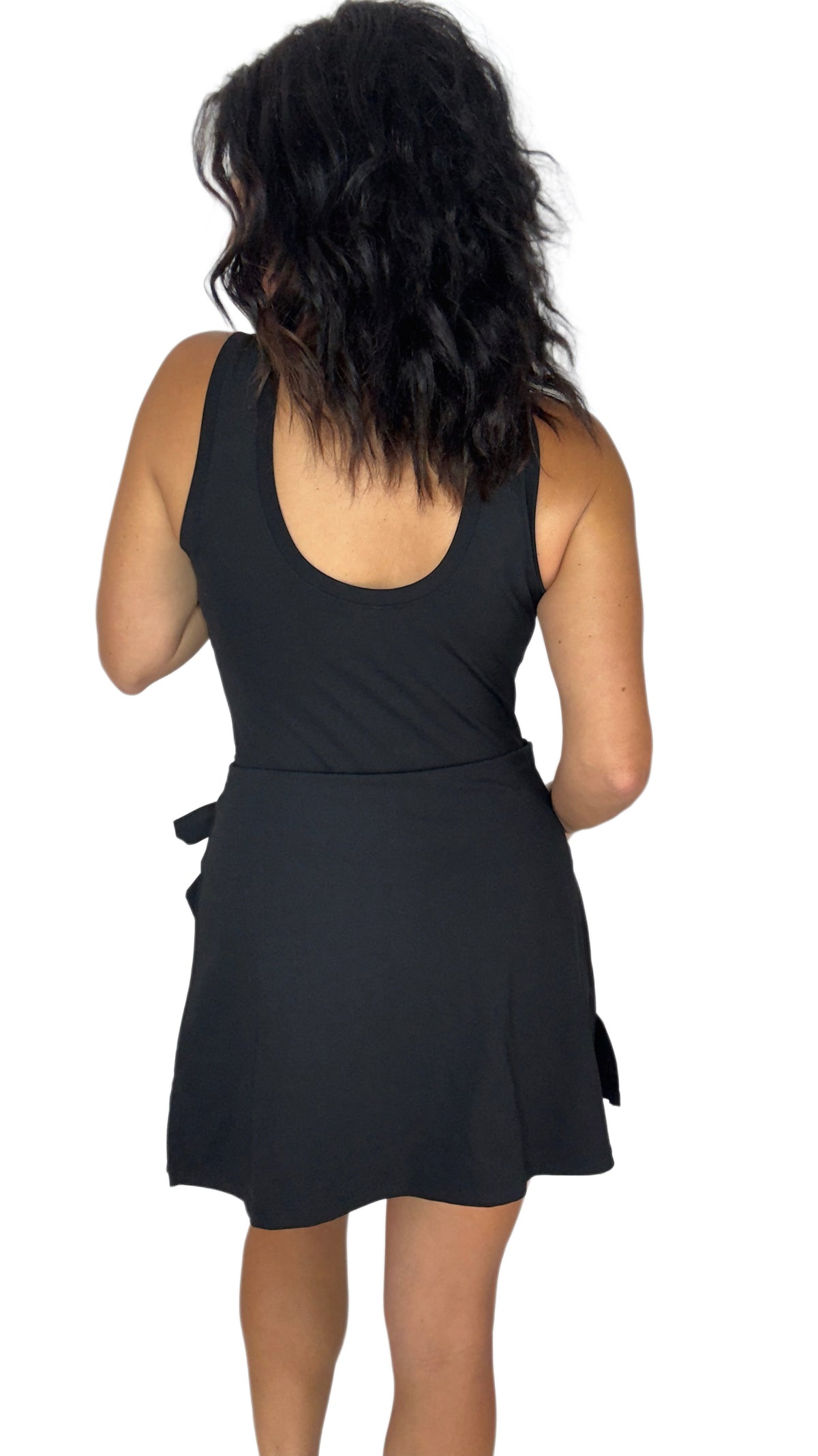 Back profile of a woman modeling a sleeveless black mini active romper  with a side-tie detail, set against a plain white background.