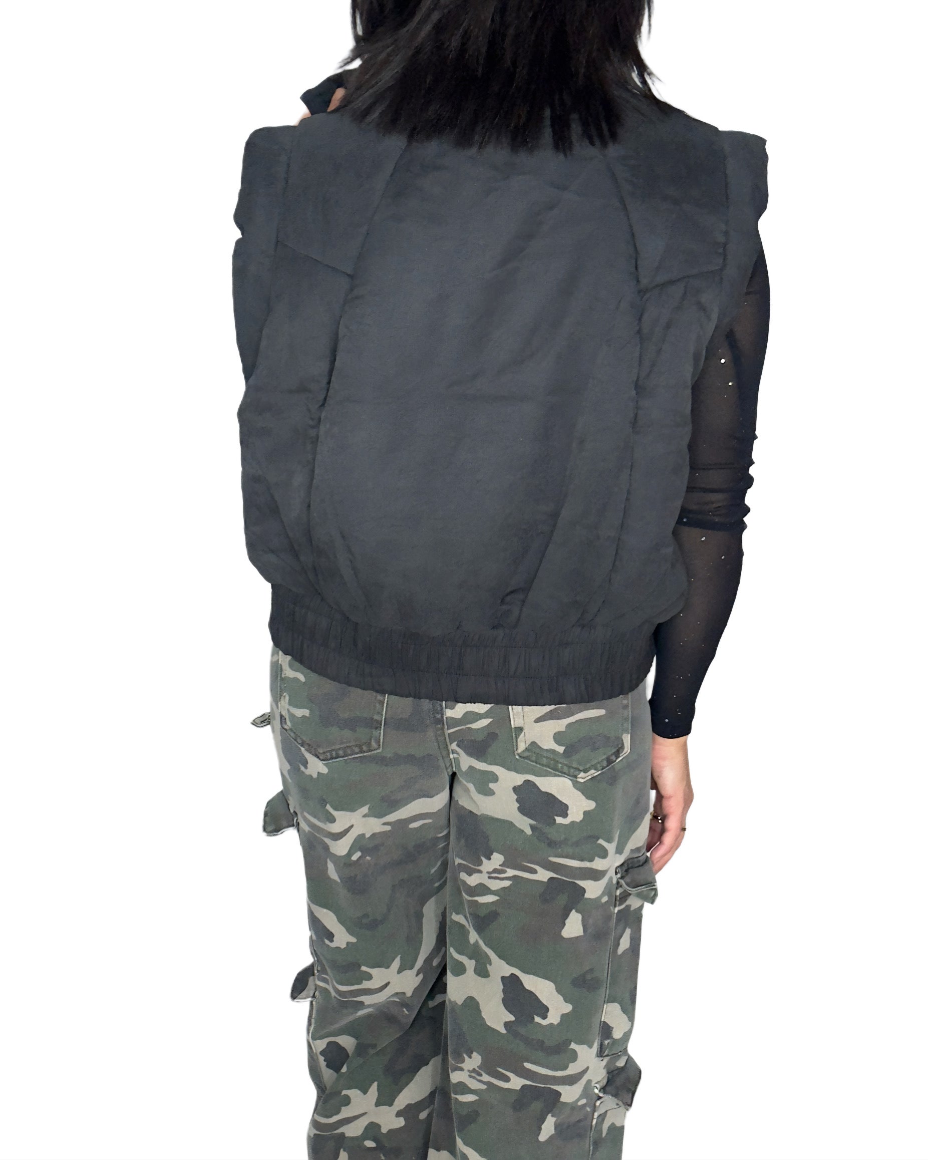 Back profile of a woman wearing a black vest and camouflage pants on a white background