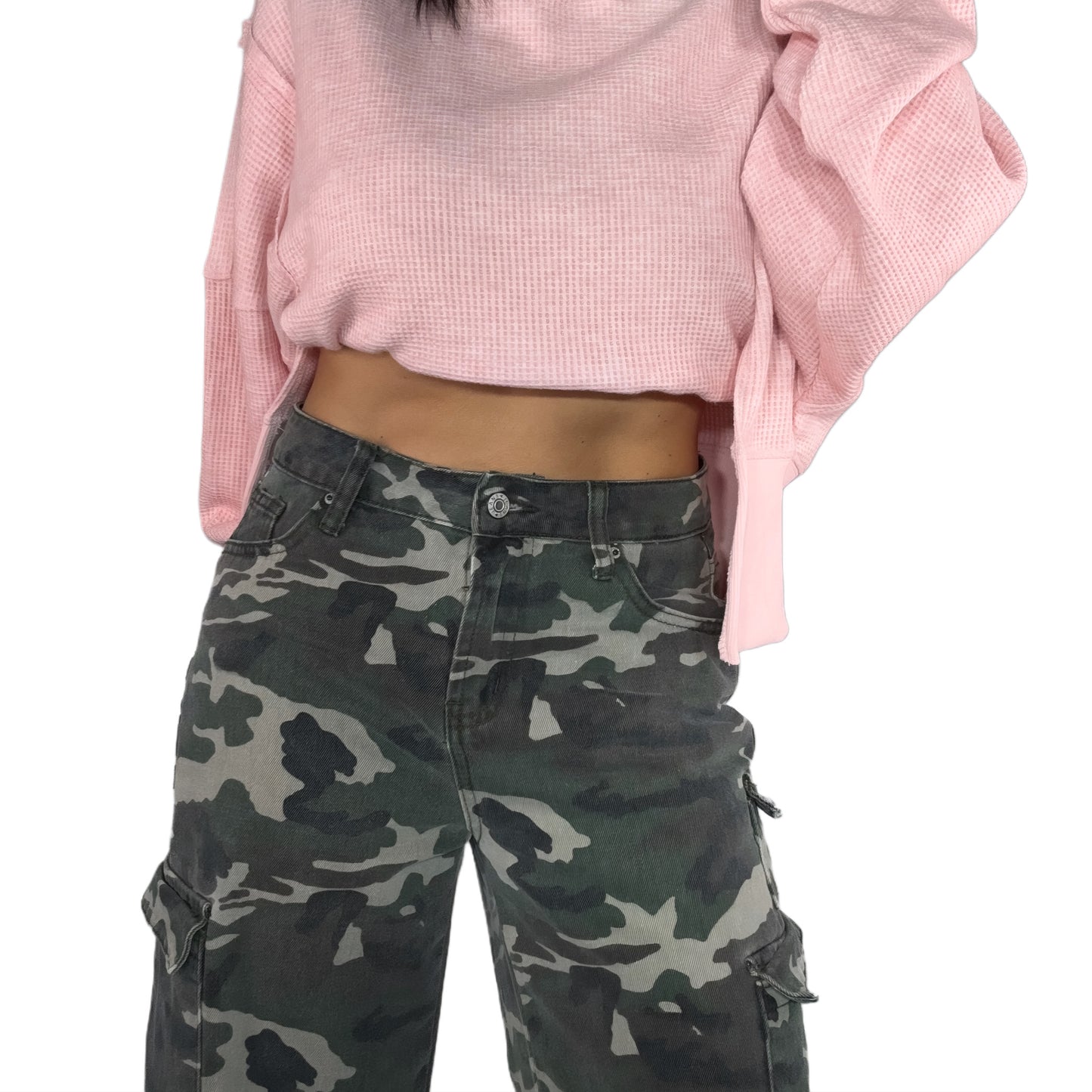 Close up of a woman wearing a pink cropped sweater and camouflage cargo pants on a white background