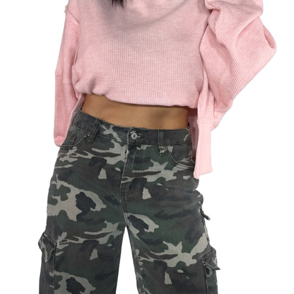 Close up of a woman wearing a pink cropped sweater and camouflage cargo pants on a white background