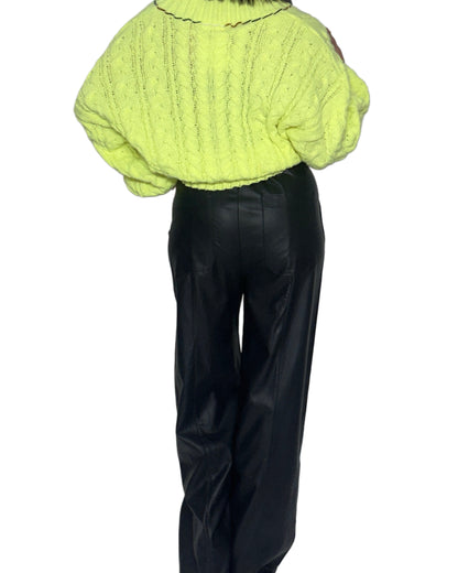 Back profile of a woman wearing a bright neon knitted sweater and black pants on a white background