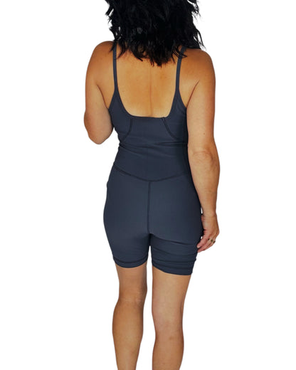 Back profile of a woman wearing a dark grey ribbed active romper on a white background