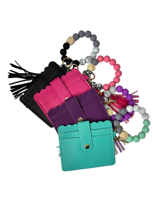 Set of colorful keychains including a turquoise cardholder, pink and purple pouches, and a beaded bracelet with tassels on a white background.