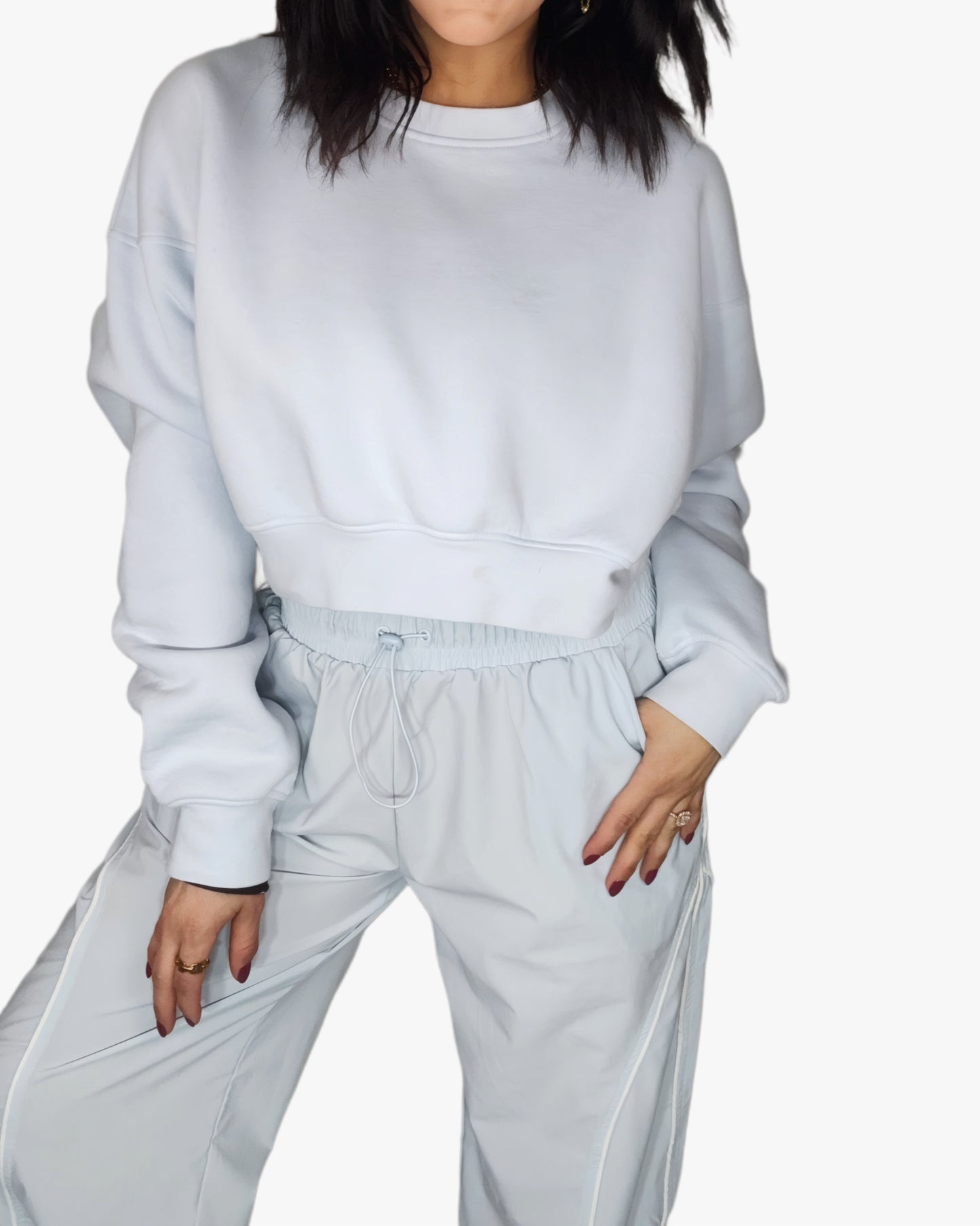 Woman wearing a light blue cropped sweatshirt with matching track pants, on a white background 