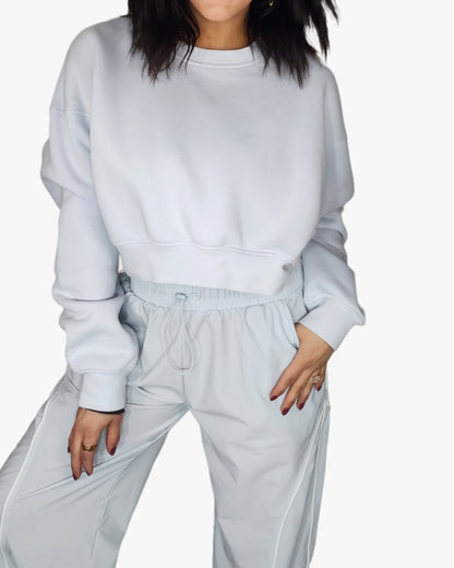 Woman wearing a light blue cropped sweatshirt with matching track pants, on a white background 