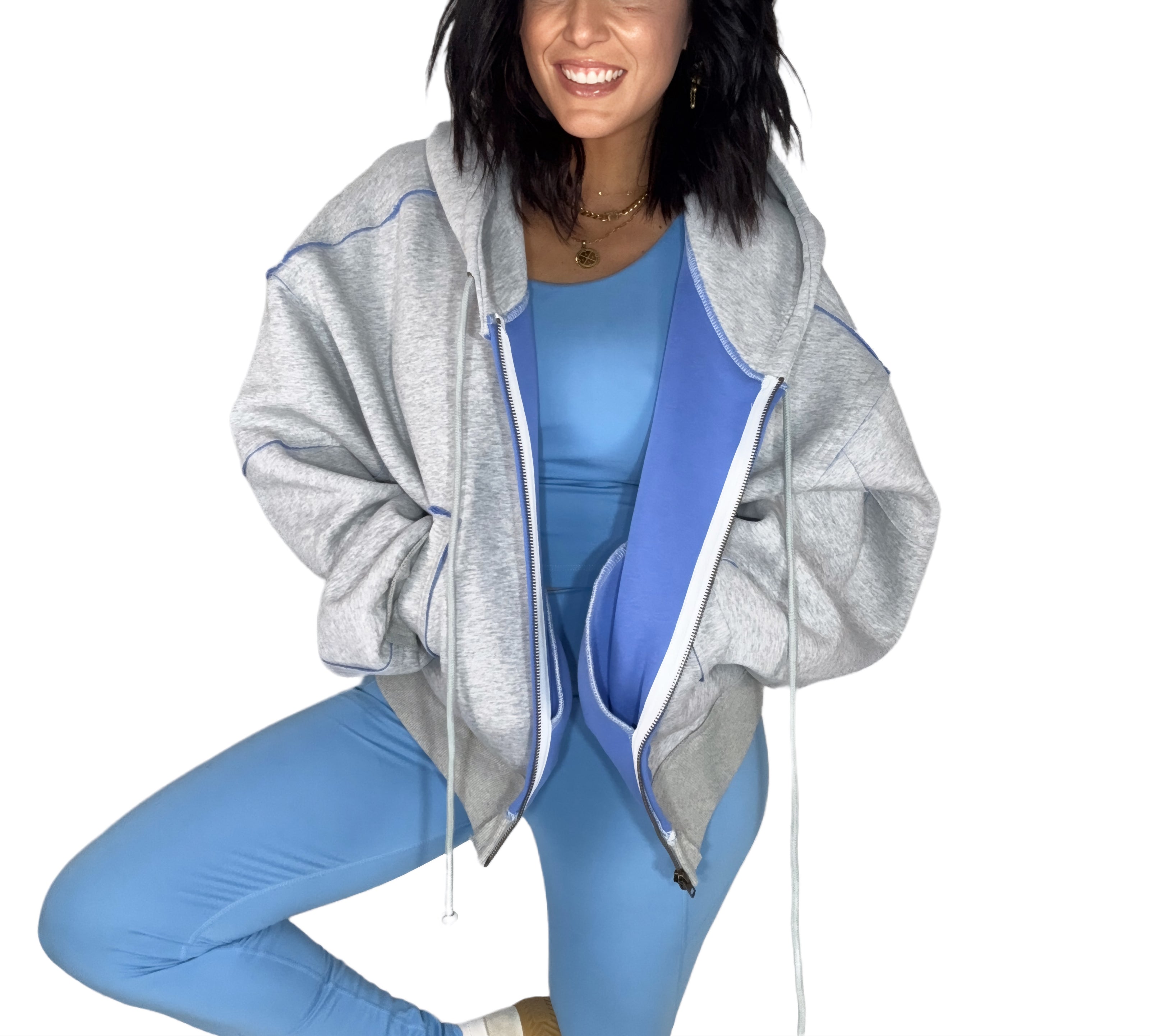 Close up of a woman wearing a gray hoodie with blue accents and matching leggings on a white background