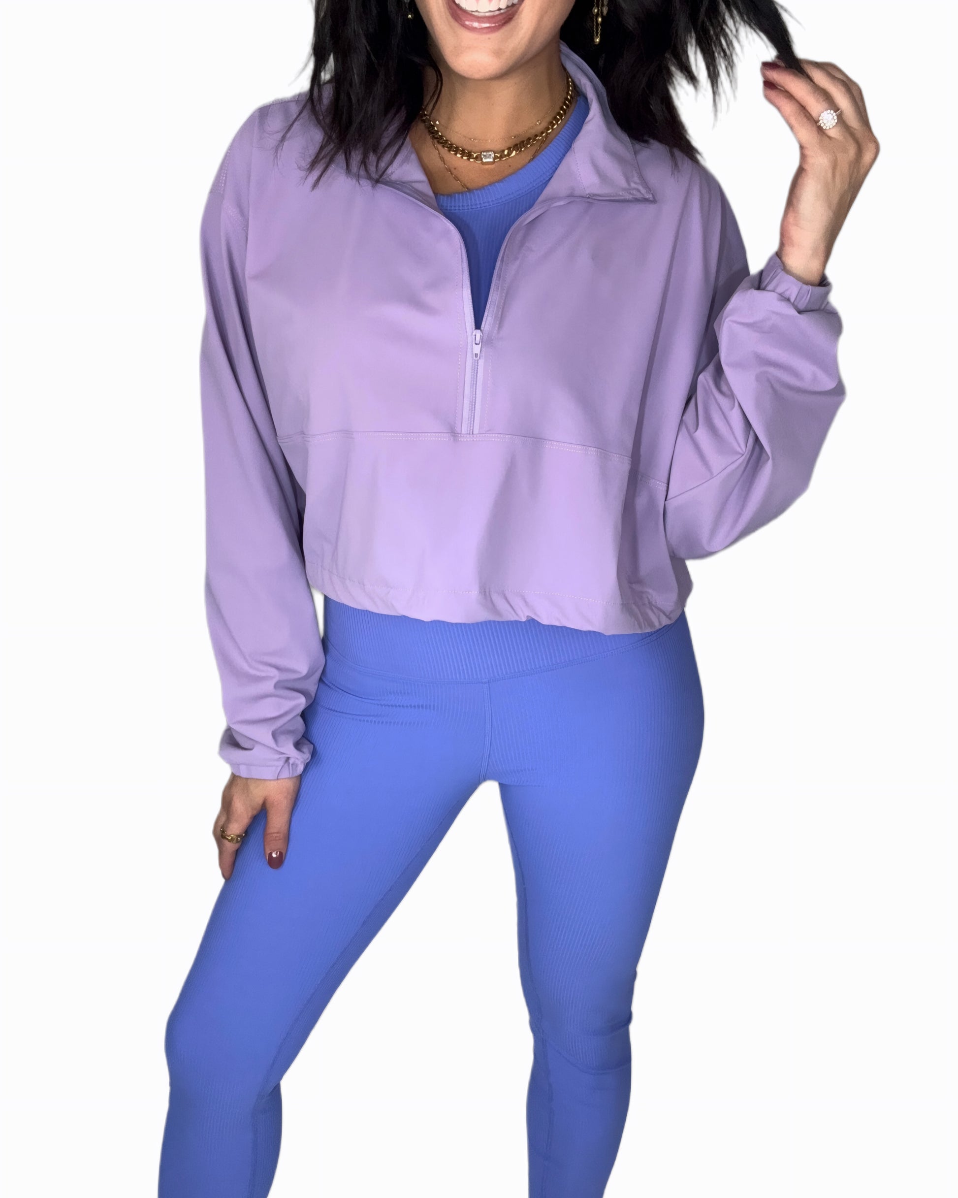 Full body photo of a woman wearing a purple half-zip jacket and blue leggings on a white background