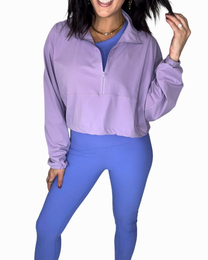 Full body photo of a woman wearing a purple half-zip jacket and blue leggings on a white background