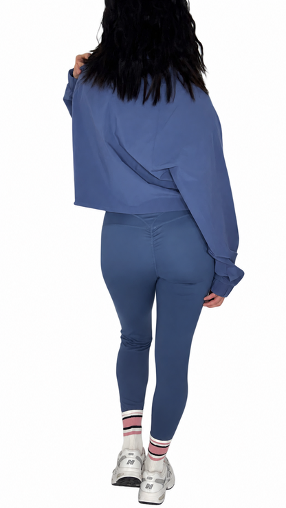 Back profile of a woman wearing blue athletic leggings with a matching jacket on a white background 