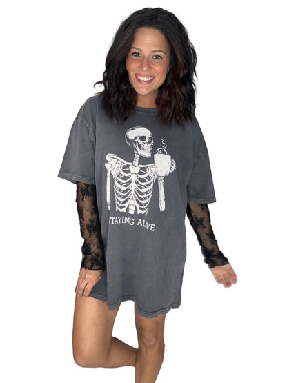 Woman wearing a deep grey Halloween skeleton tee that says "staying alive" with a lace undershirt on white background 