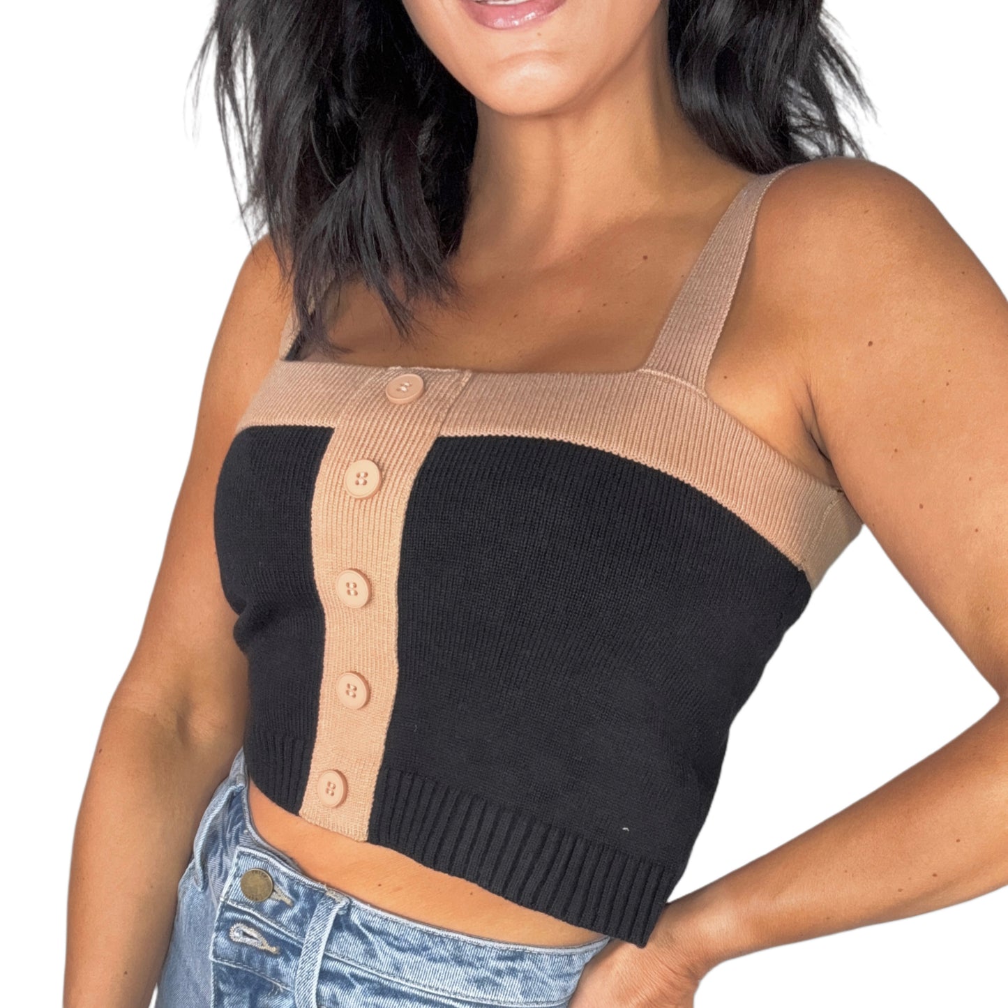 Side profile of a woman wearing a black and beige button-up crop top with high-waisted jeans on a white background
