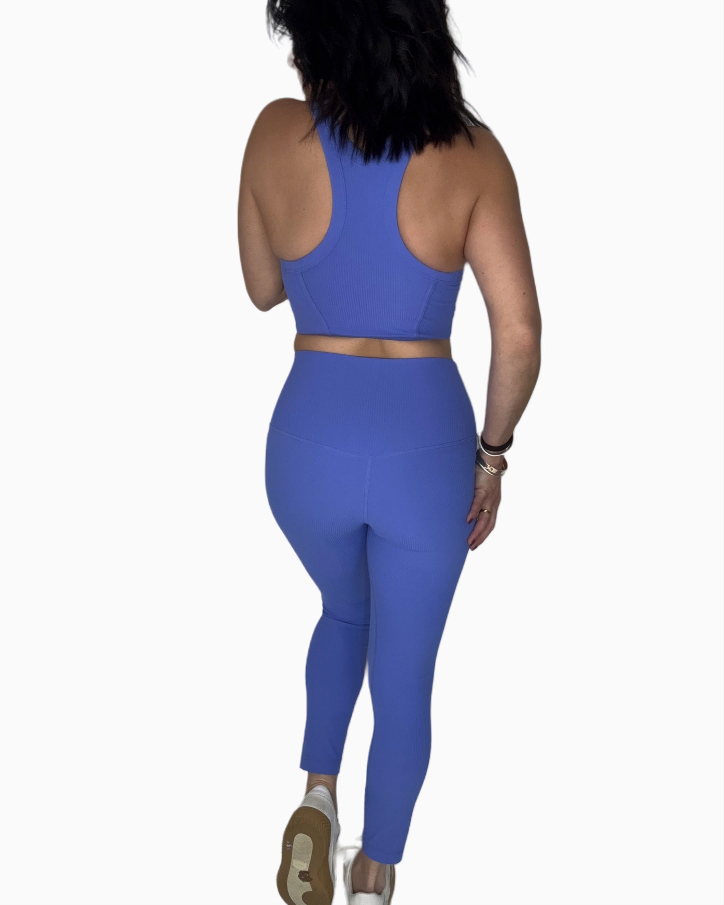 Back profile of a woman wearing wearing a ribbed blue athletic outfit on a white background