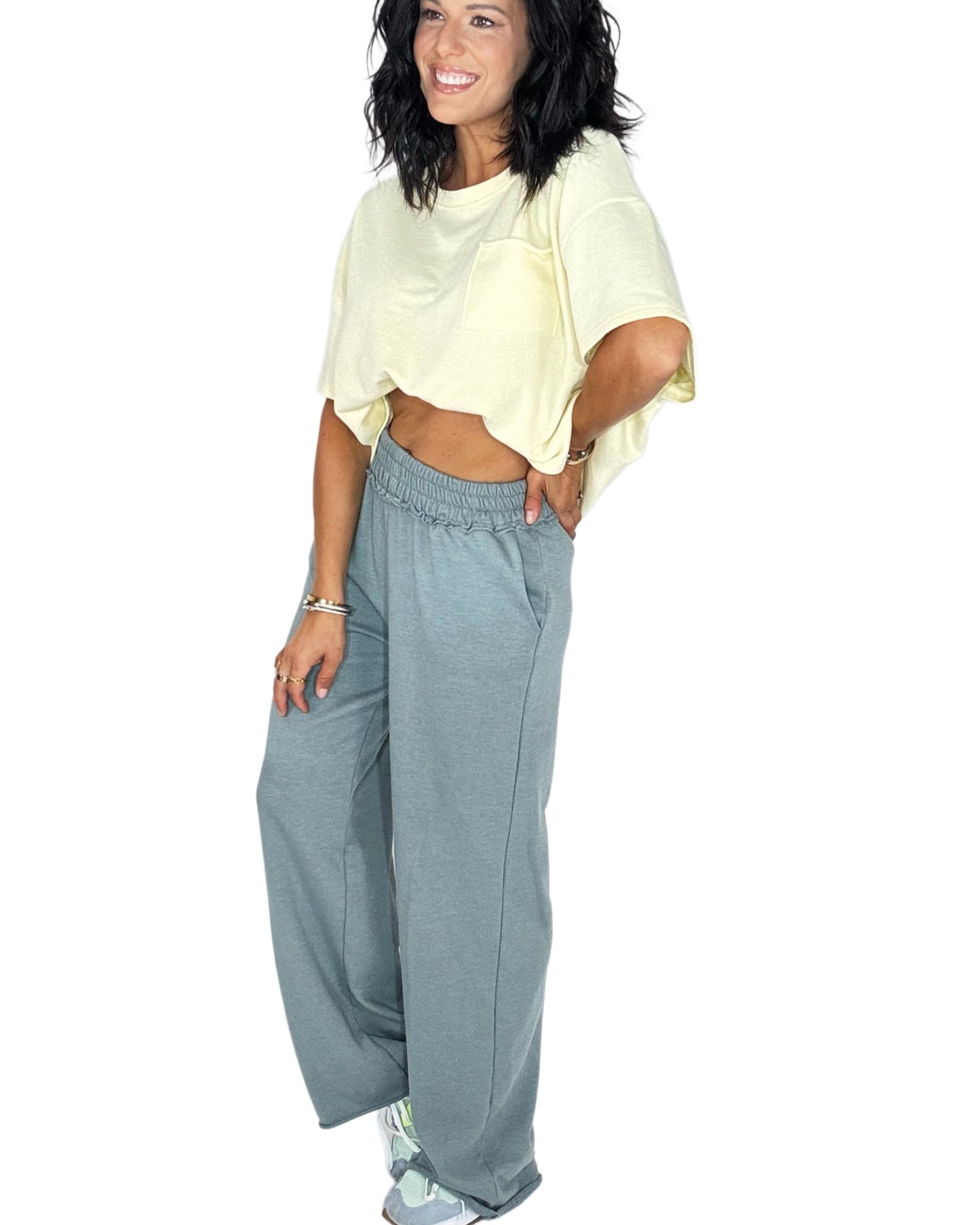 Side profile of a woman wearing blue grey sweat pants with a yellow tee on a white background