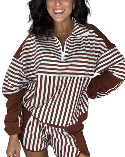 A woman wearing a brown and white striped long-sleeve top with a half-zip collar and matching striped shorts, shown against a plain white background.