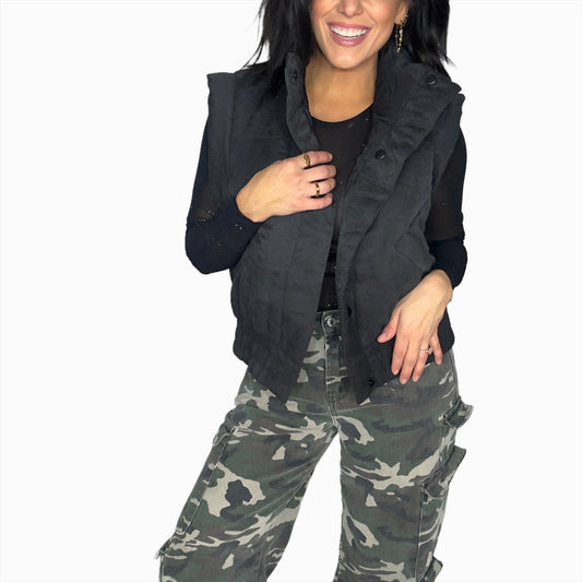 Woman wearing a black vest over a black shirt with camouflage pants on a white background