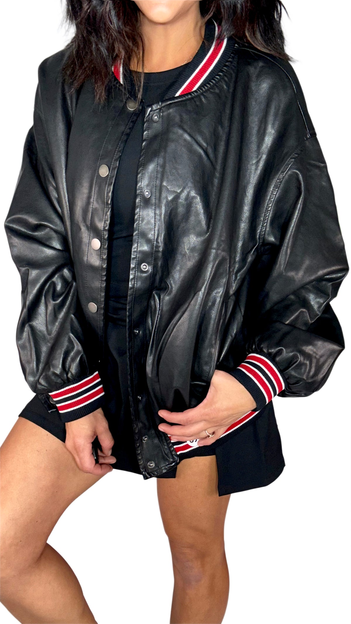 Side profile of a woman modeling a black faux-leather varsity jacket with red and white striped ribbed collar, cuffs, and hem, paired with black shorts against a plain white background.