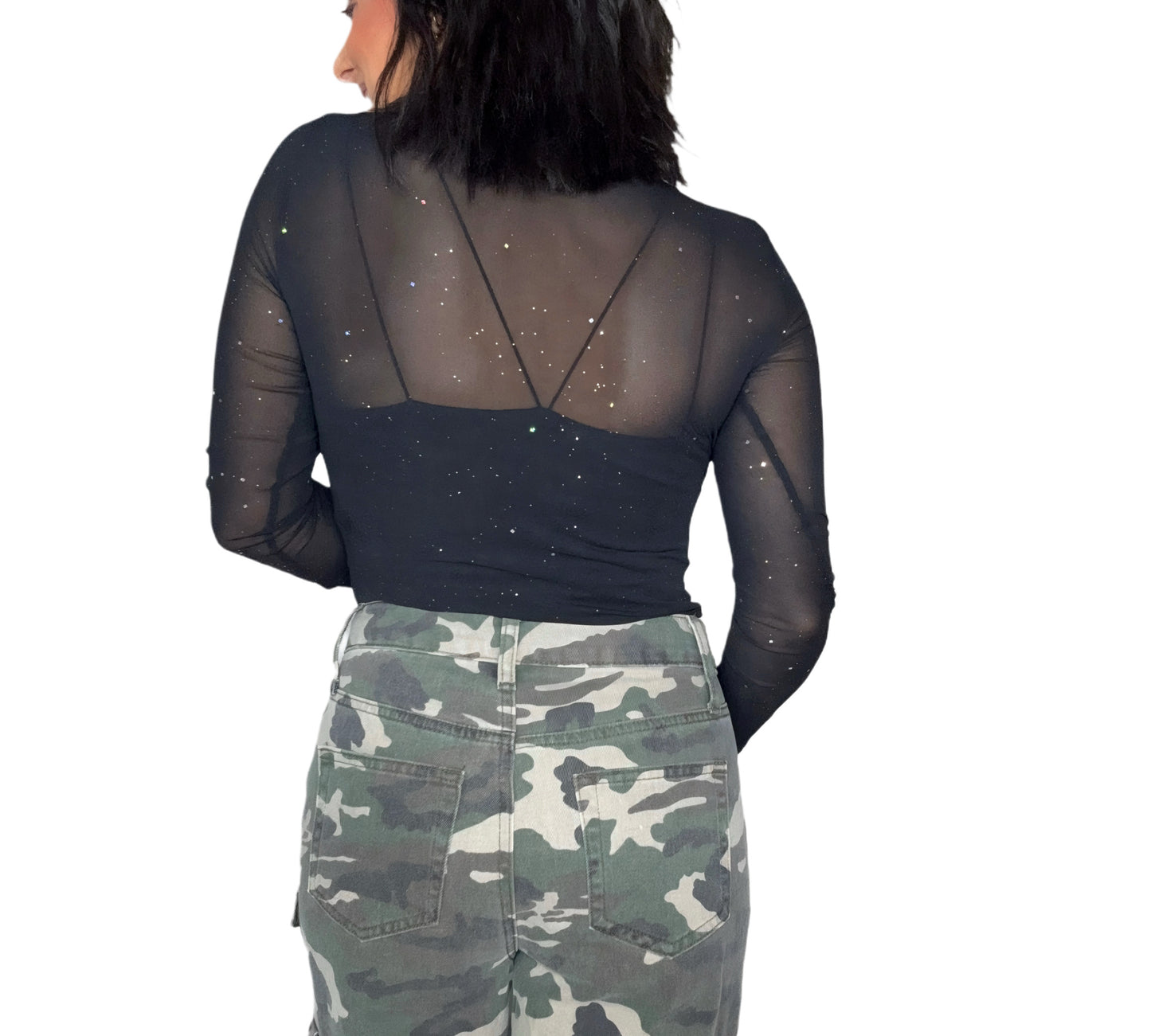 Back profile on a woman wearing a black sheer top with silver speck patterns and camouflage pants on a white background