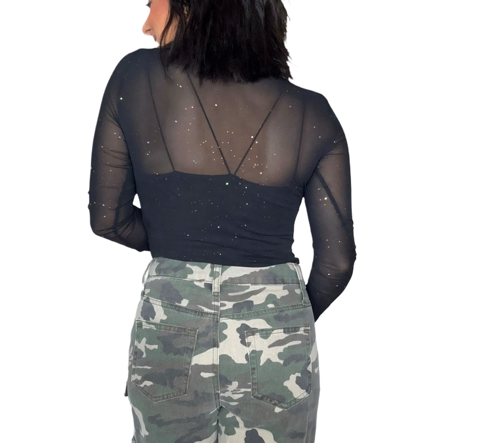 Back profile on a woman wearing a black sheer top with silver speck patterns and camouflage pants on a white background