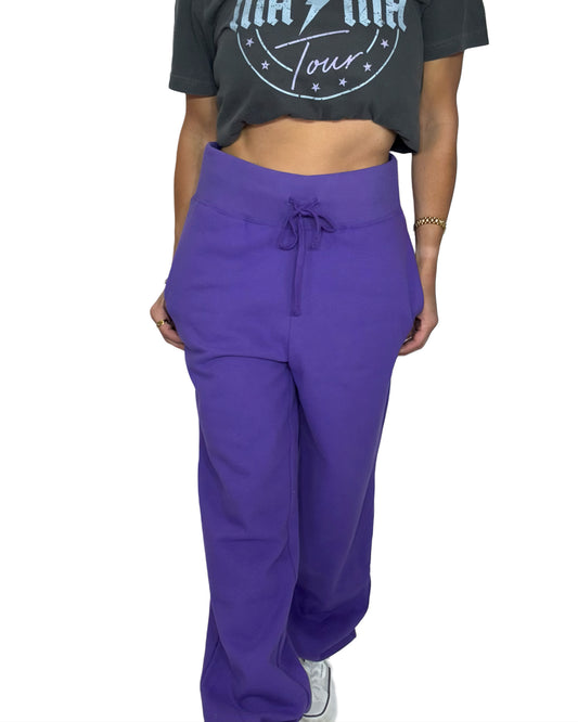 Woman wearing purple joggers with a graphic tee and white background 