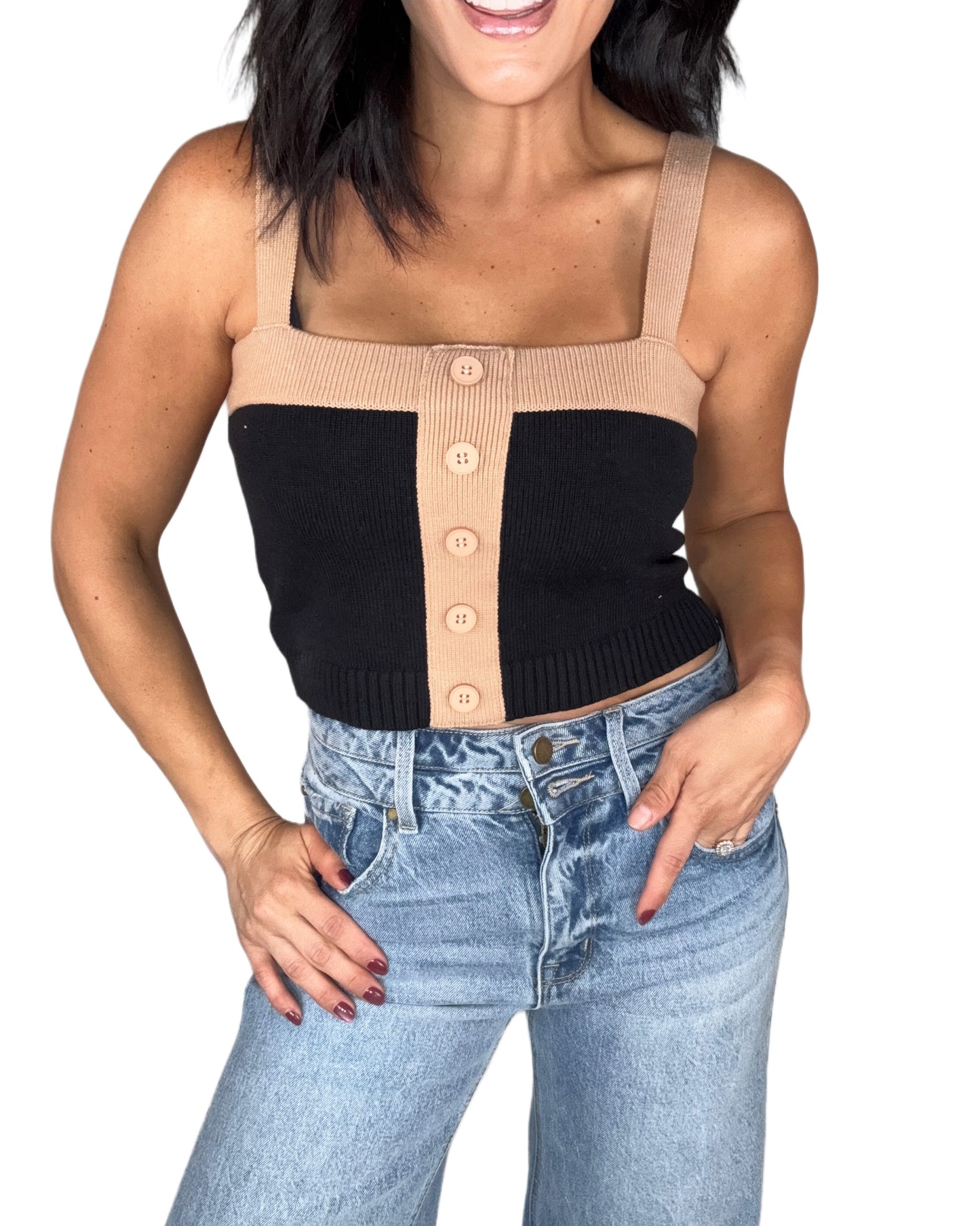 Woman wearing a black and beige button-up crop top with high-waisted jeans on a white background