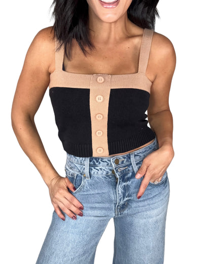 Woman wearing a black and beige button-up crop top with high-waisted jeans on a white background