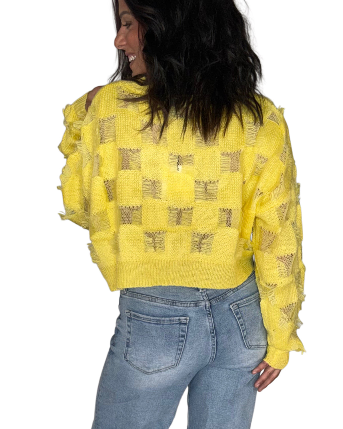 Back profile of a woman wearing a yellow relaxed fit sweater top with distressed details, paired with medium washed jeans on a white background