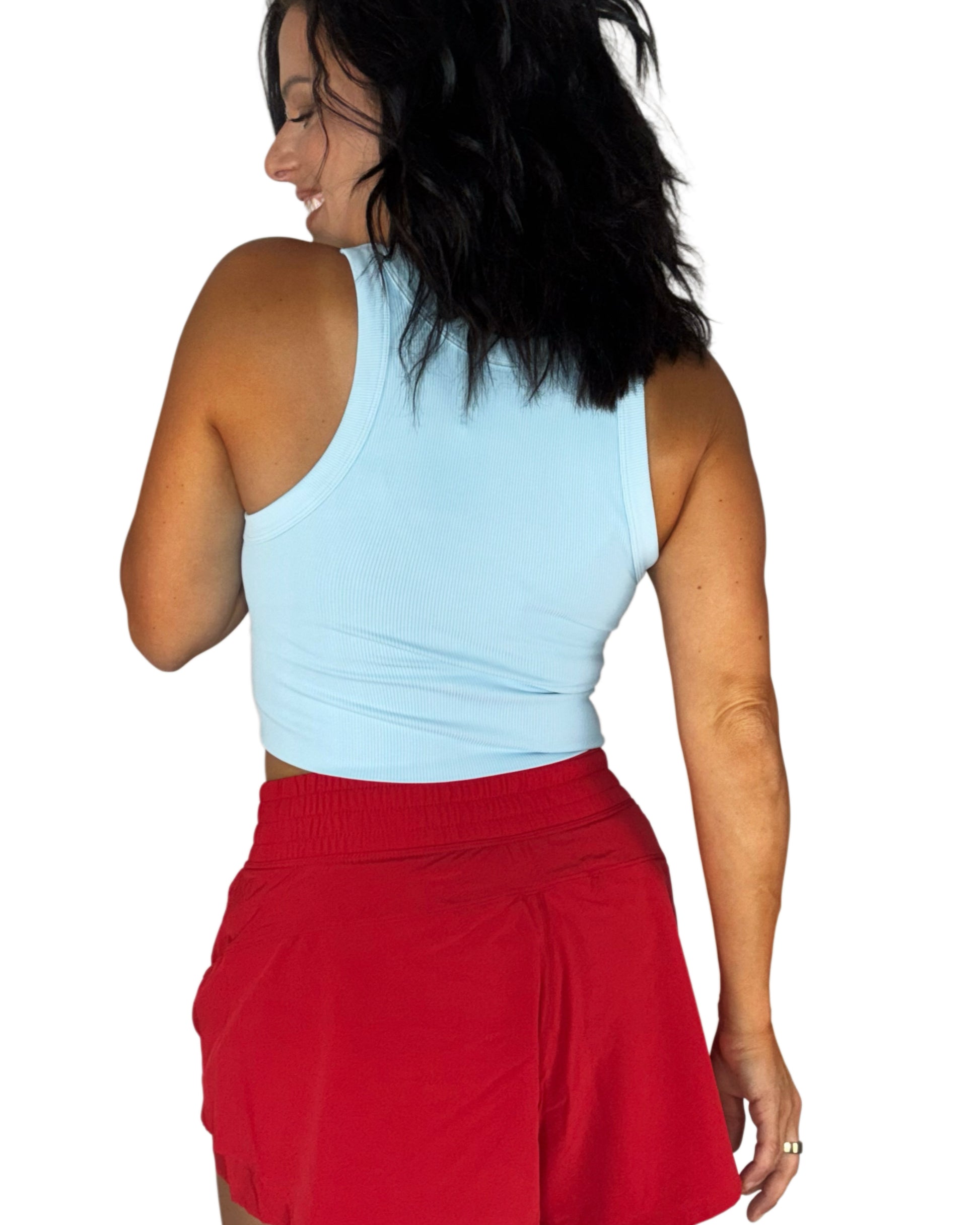 Back profile of a woman wearing a ribbed sky blue tank and red active shorts on a white background