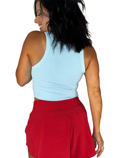 Back profile of a woman wearing a ribbed sky blue tank and red active shorts on a white background