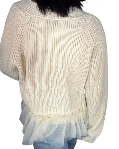 Back profile of a woman wearing a cream cardigan with tulle at the bottom and jeans on a white background