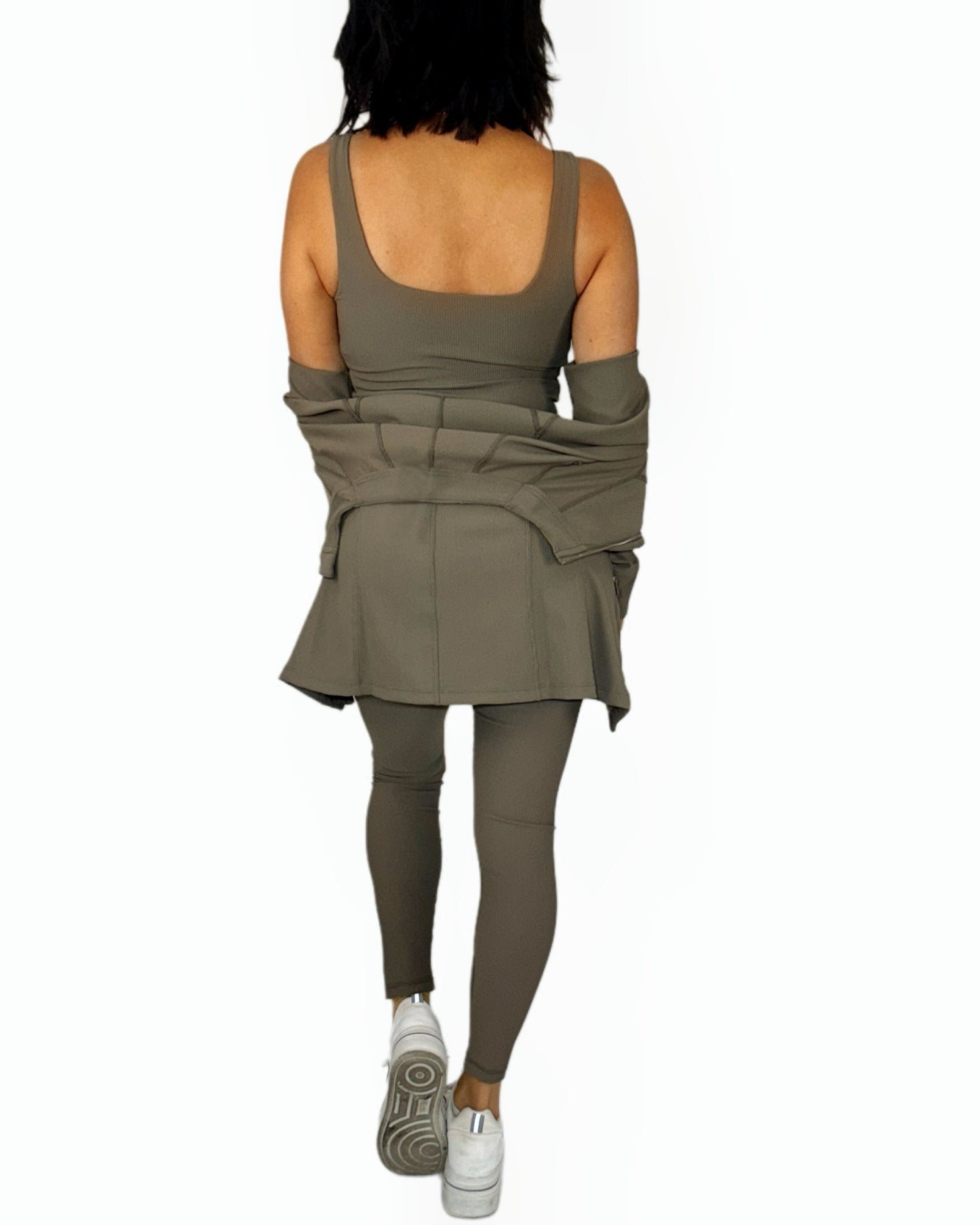 Back profile of a woman wearing a three piece green ribbed athletic set on a white background 