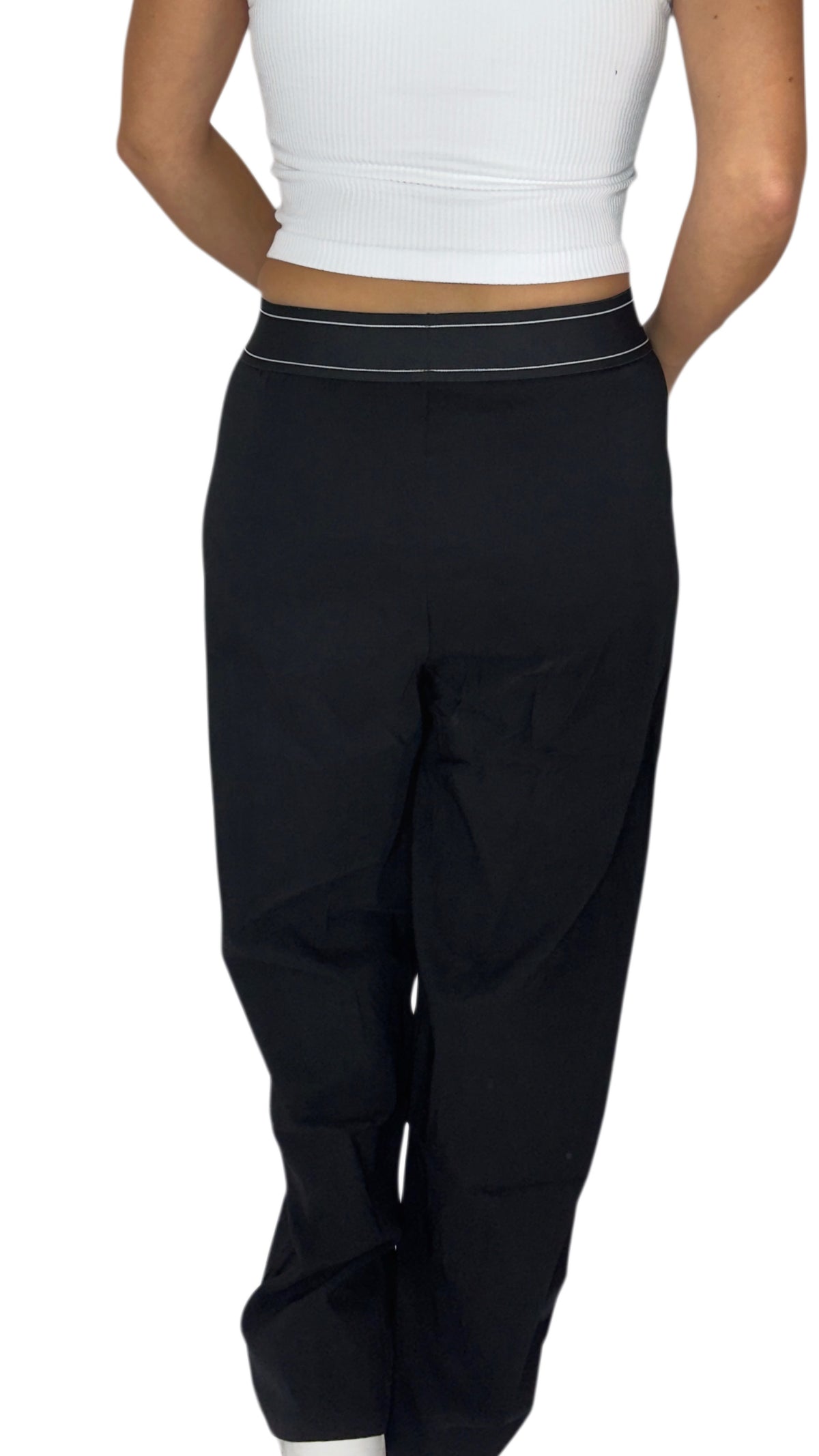 Back profile of a woman modeling a pair of navy blue wide-leg sweatpants with a thin white stripe detail along the waistband, paired with a white crop top and white sneakers, against a plain white background.