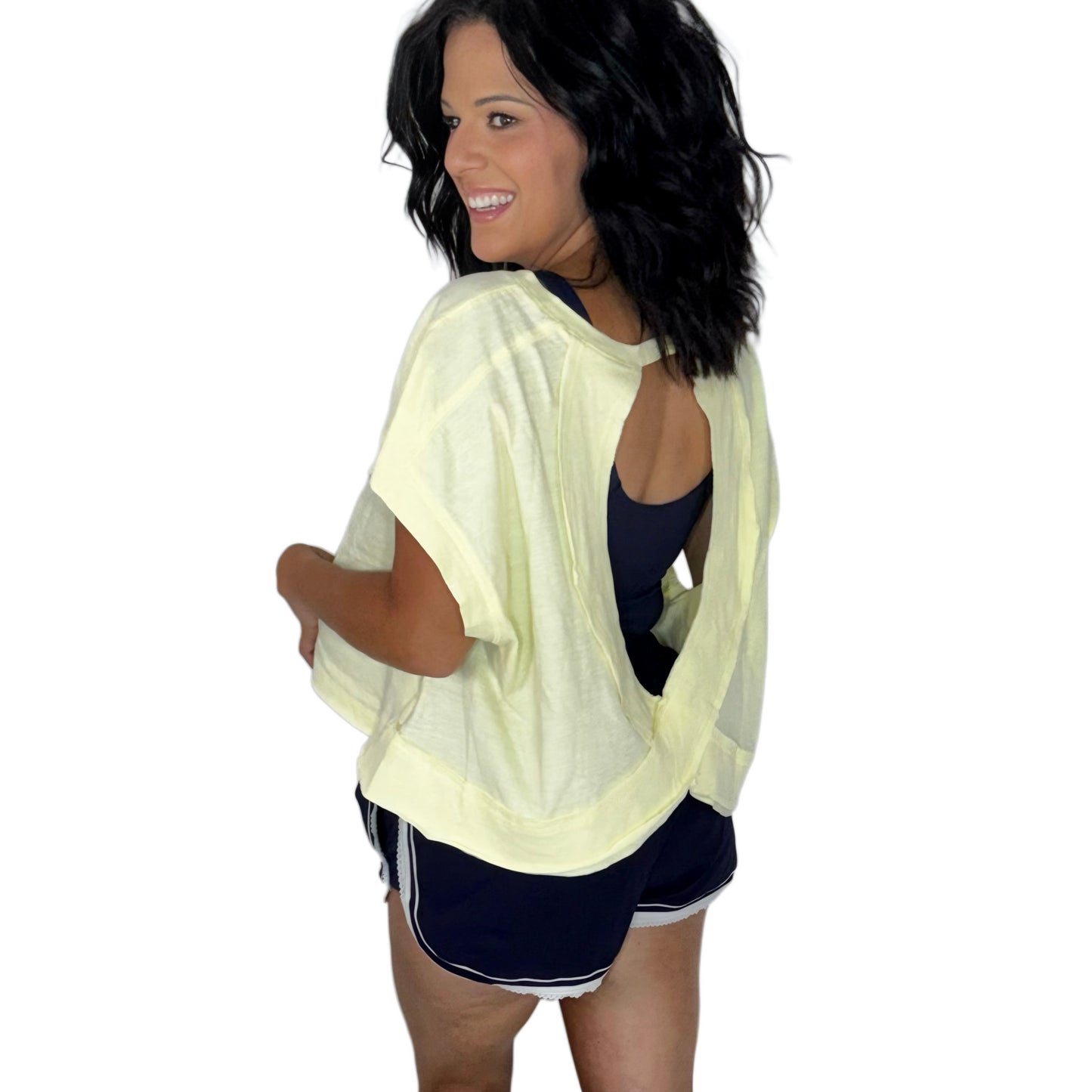 Woman wearing a pale yellow top with a key hole on the back, paired with navy shorts and navy tank on a white background